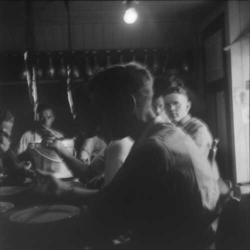 Zeven soldaten zittend en etend aan tafel in de blokhut in Aarle-Rixtel; één staande soldaat die uit een beker drinkt. De meesten zijn in onderkleding. (Foto: Johan Prinsen, Collectie familie Prinsen, 1939)